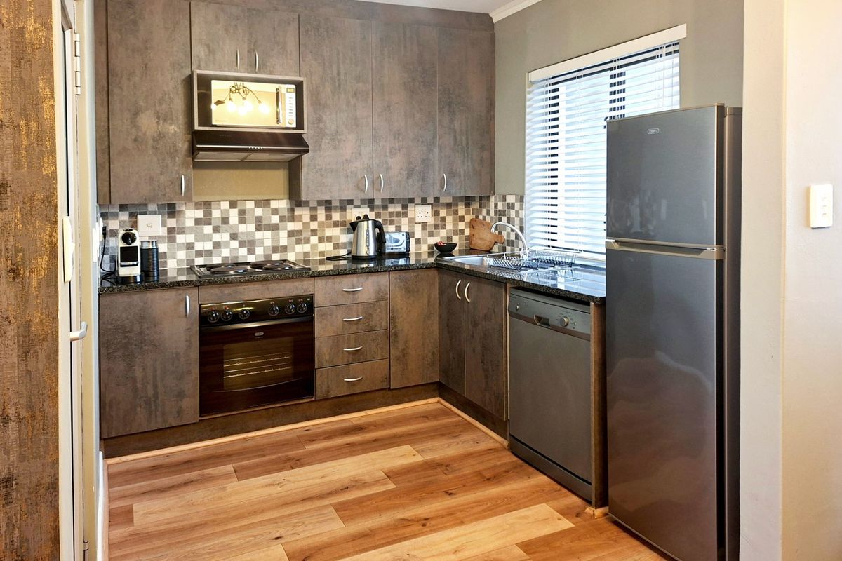 Modern kitchen featuring dark textured cabinetry, granite countertops, mosaic backsplash, built-in oven, hob, extractor fan, and integrated microwave with laminate flooring.