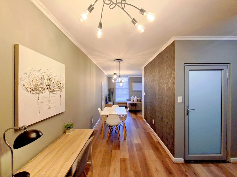An open-plan living and dining area featuring laminate flooring, a textured feature wall, and contemporary pendant lighting, leading to a bright lounge space.