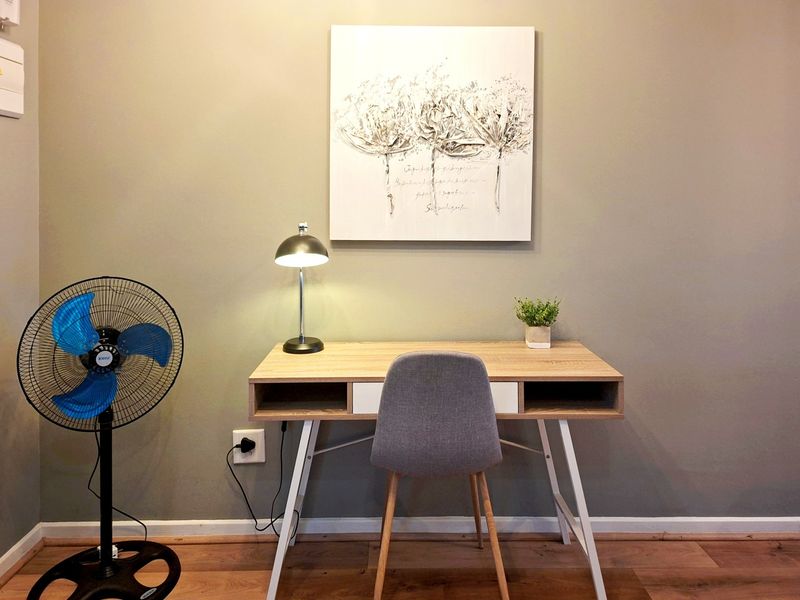 A well-maintained home office space featuring neutral wall tones, laminate flooring, and a dedicated electrical outlet for workspace connectivity.