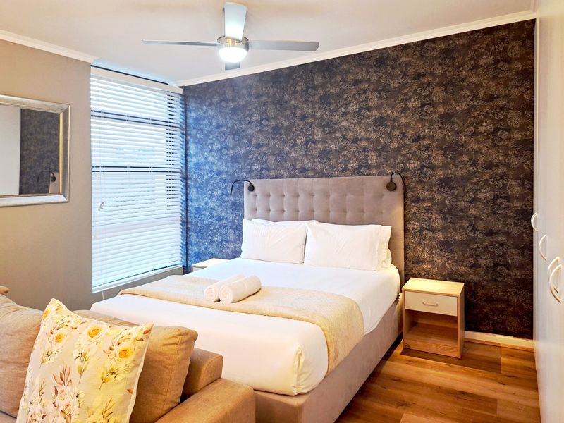 A well-maintained bedroom featuring laminate flooring, a ceiling fan, venetian blinds, and a built-in wardrobe with a decorative feature wall.
