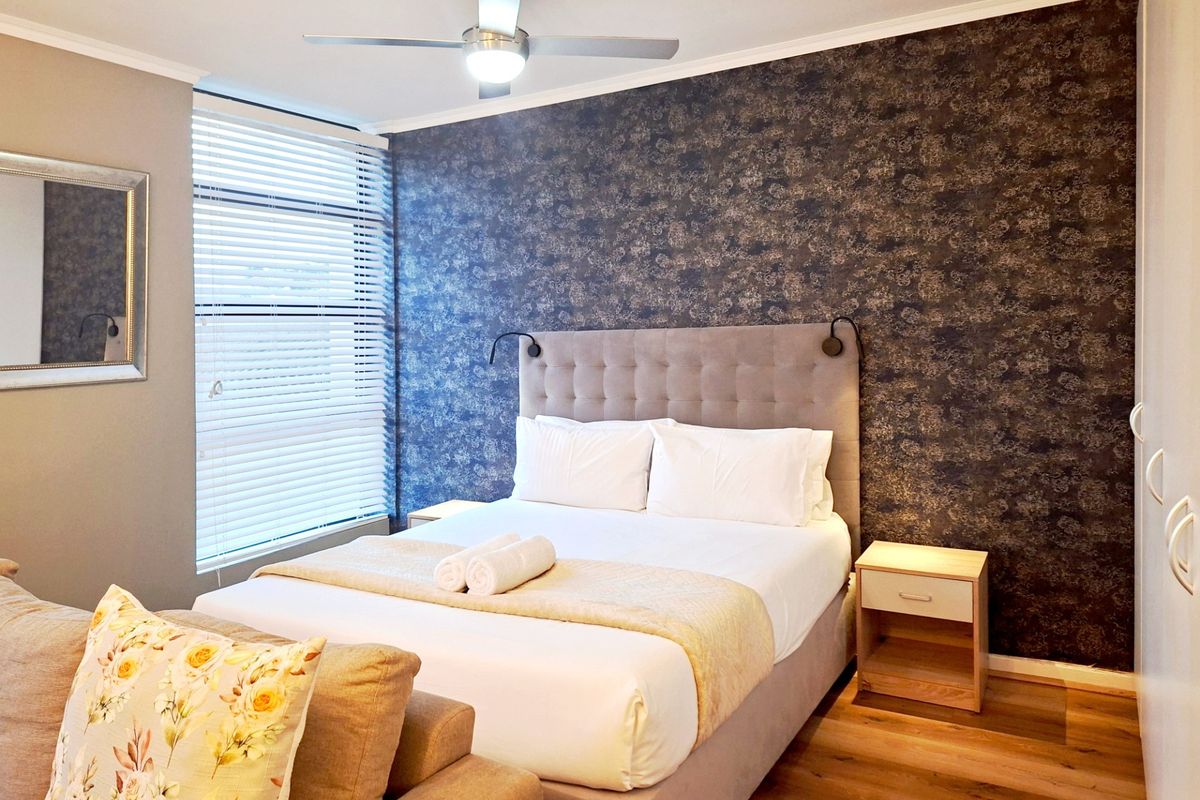 A well-maintained bedroom featuring laminate flooring, a ceiling fan, venetian blinds, and a built-in wardrobe with a decorative feature wall.