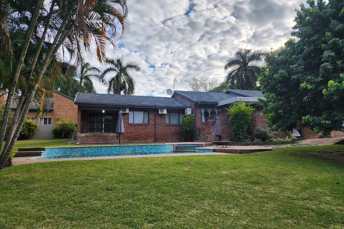 Rear view of the property featuring a brick facade, tiled roof, and a swimming pool set within a well-maintained garden.
