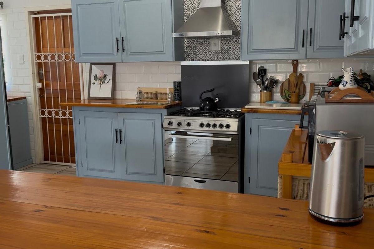 A functional kitchen featuring blue cabinetry, wooden countertops, a gas stove with an extractor fan, and a decorative tiled backsplash.