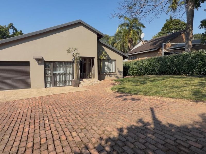 Front exterior view of the house featuring a paved driveway, single garage, and well-maintained garden area with established hedging.