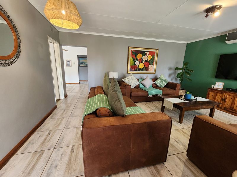 A spacious living room featuring light-toned tiled flooring, a feature green accent wall, and an integrated air conditioning unit.