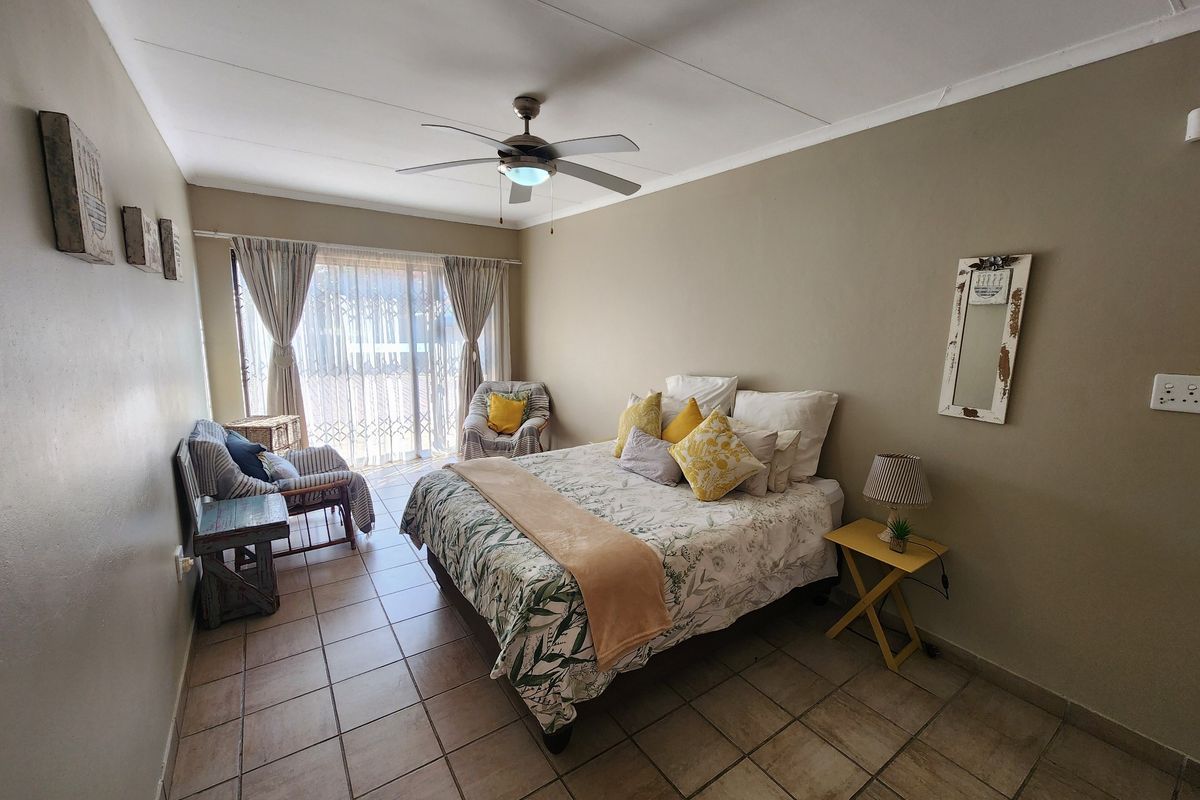 A spacious bedroom featuring tiled flooring, a ceiling fan, and a sliding glass door providing access to the exterior.