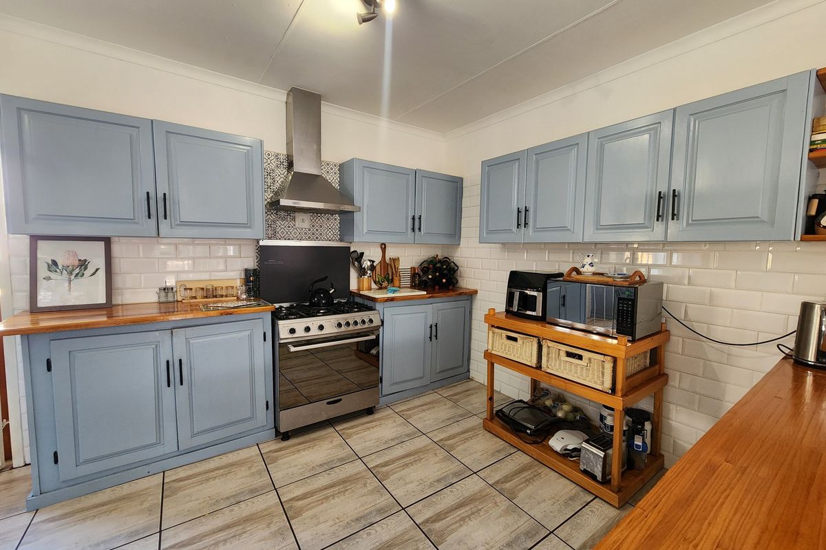 A well-maintained kitchen featuring light blue cabinetry, wooden countertops, a stainless steel extractor fan, and a classic subway tile backsplash.