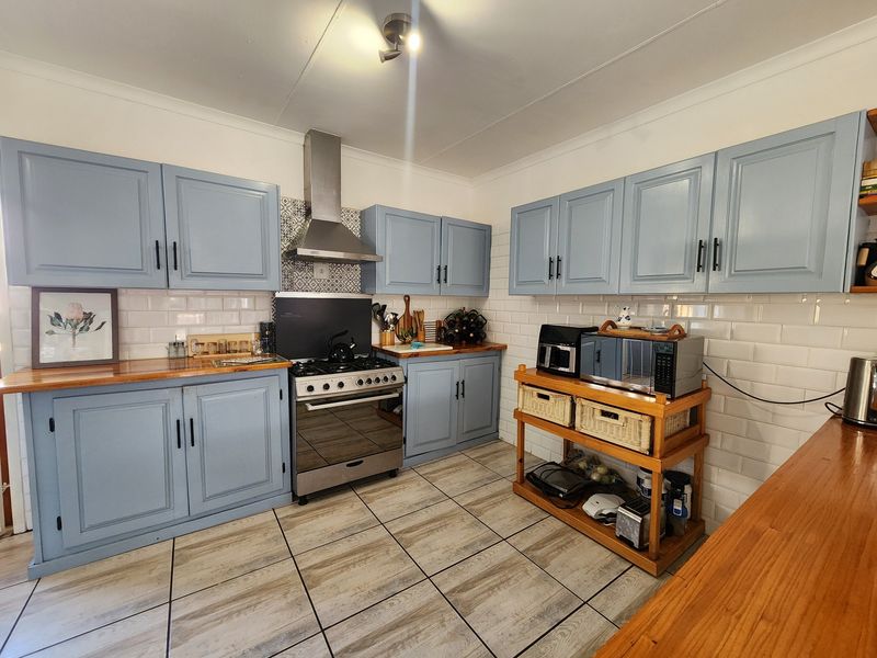 A well-maintained kitchen featuring light blue cabinetry, wooden countertops, a stainless steel extractor fan, and a classic subway tile backsplash.