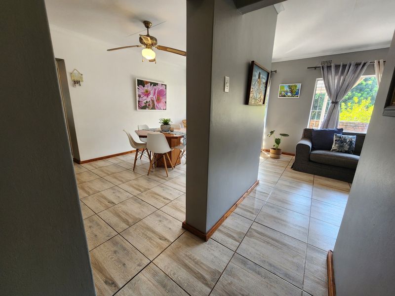 An open-plan living and dining area featuring neutral tiled flooring, a central ceiling fan, and a partition wall separating the two functional spaces.