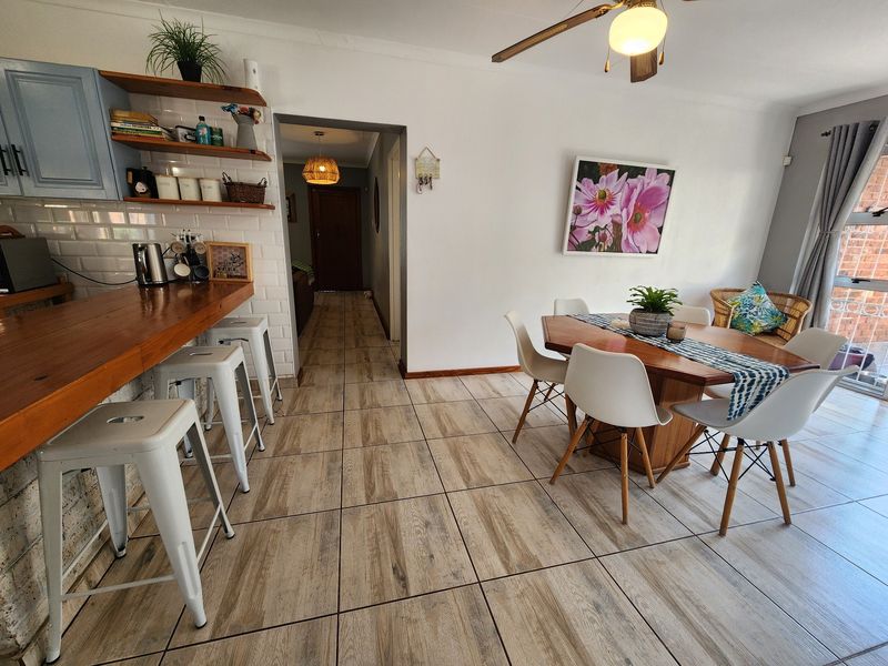 Open plan living and dining area featuring wood-look ceramic floor tiles, a breakfast bar with subway tile backsplash, and a ceiling fan.
