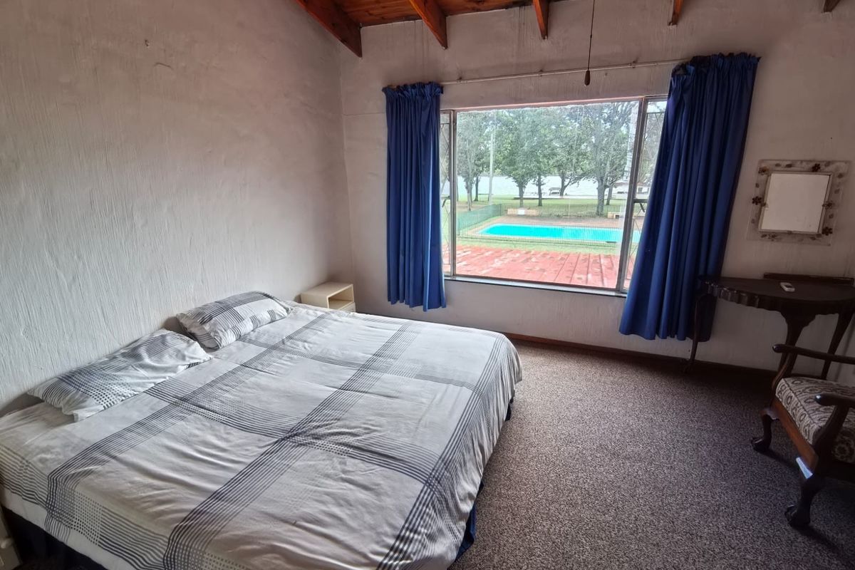 Spacious bedroom featuring exposed timber beam ceilings, large picture window with pool views, and carpeted flooring.