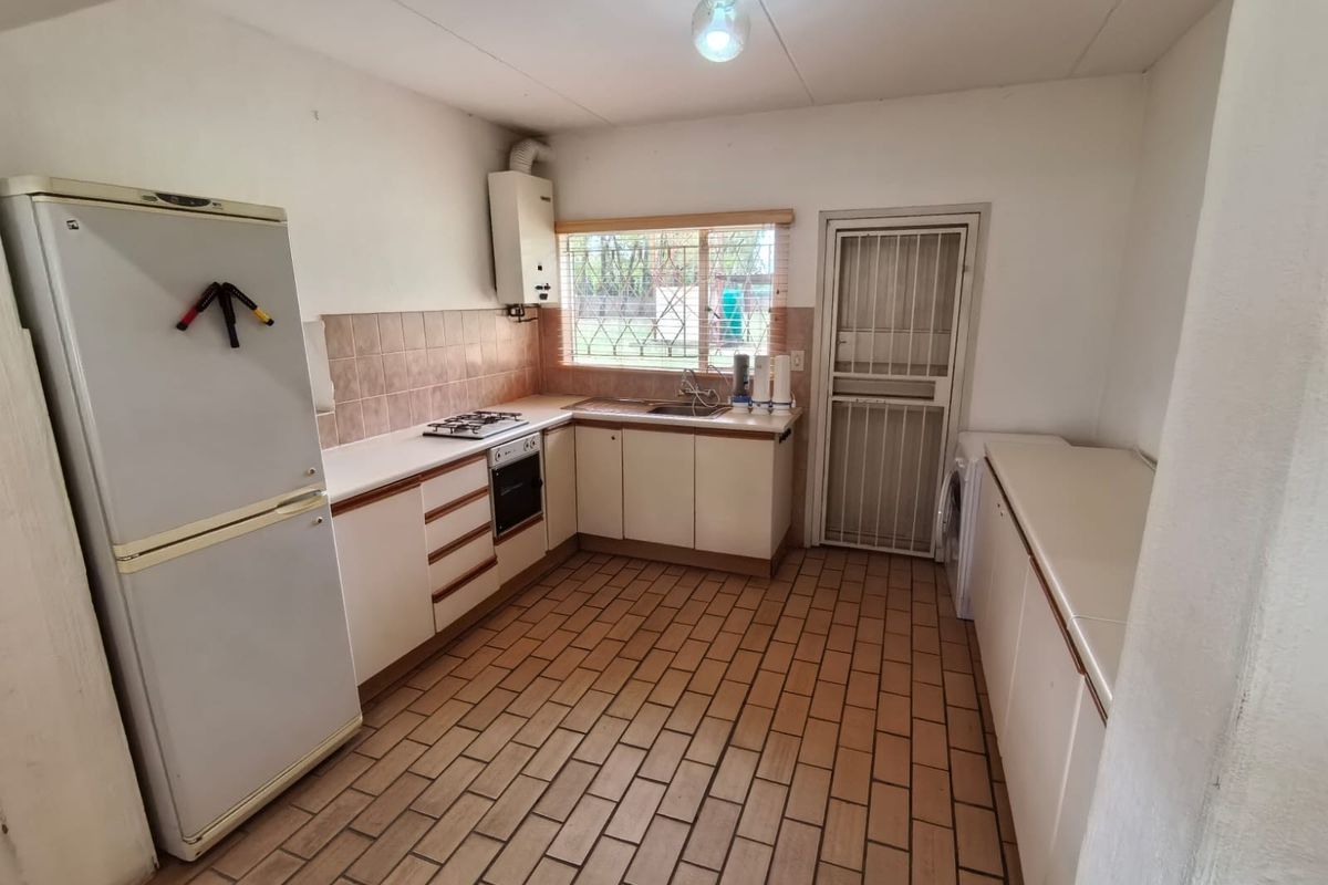 Functional kitchen featuring built-in cabinetry, gas hob, oven, and tiled flooring, with direct access to the exterior via a security gate.