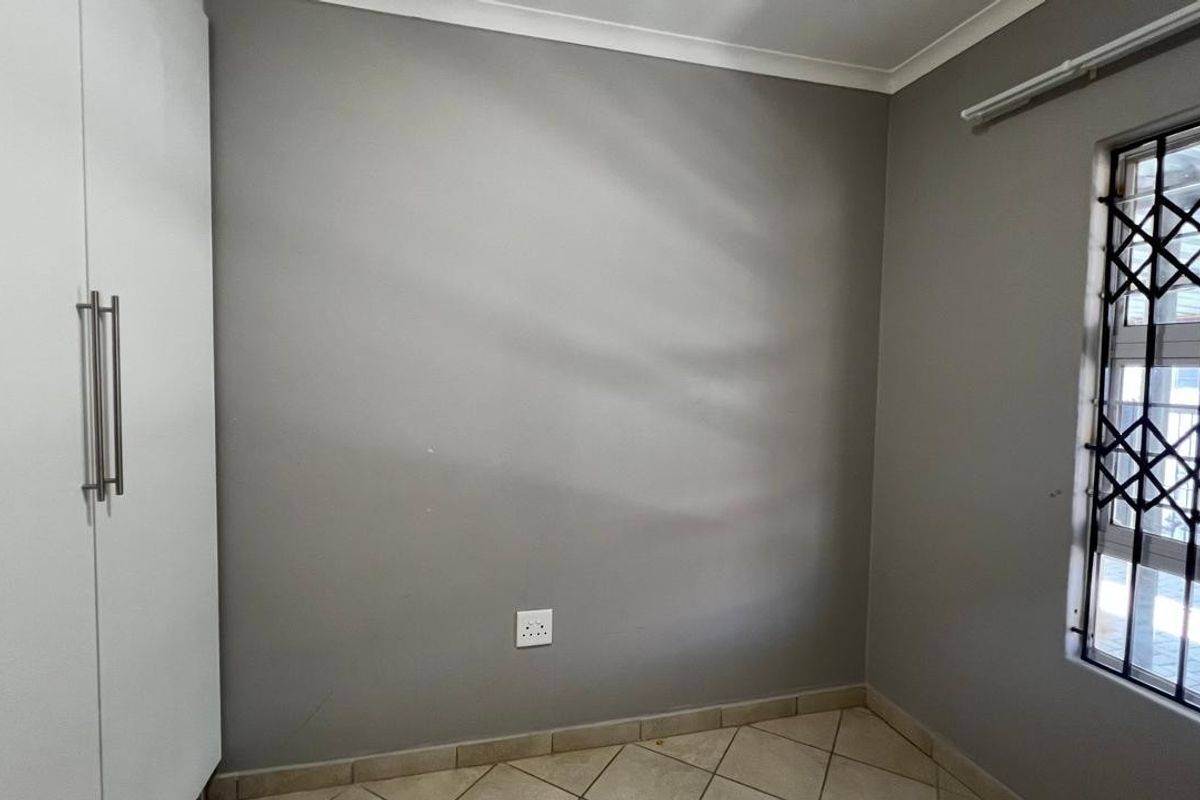 A clean, empty bedroom featuring neutral grey walls, tiled flooring, and a built-in cupboard with a secure window.