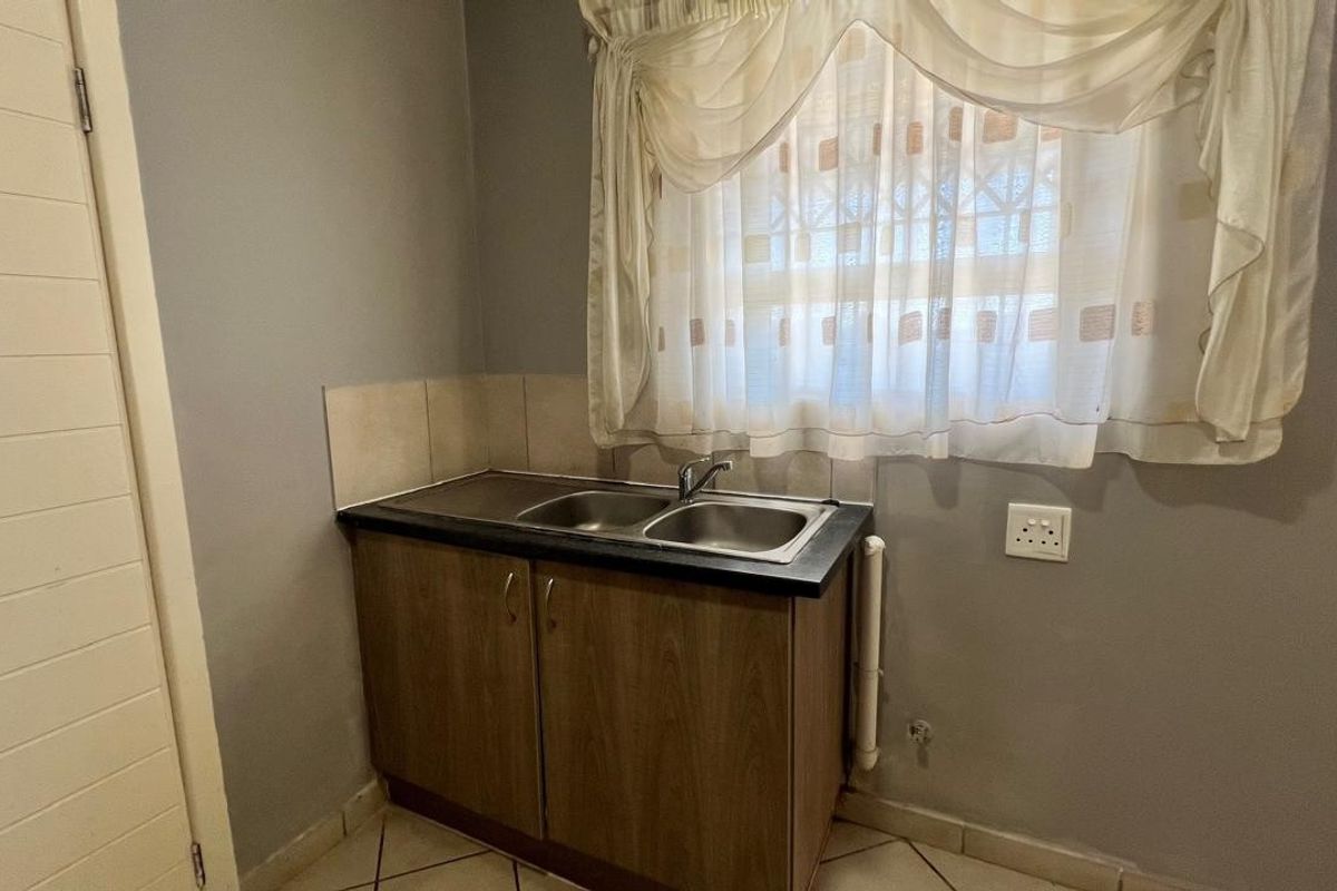 A functional laundry area featuring a stainless steel double sink, laminate cabinetry, and tiled splashback.