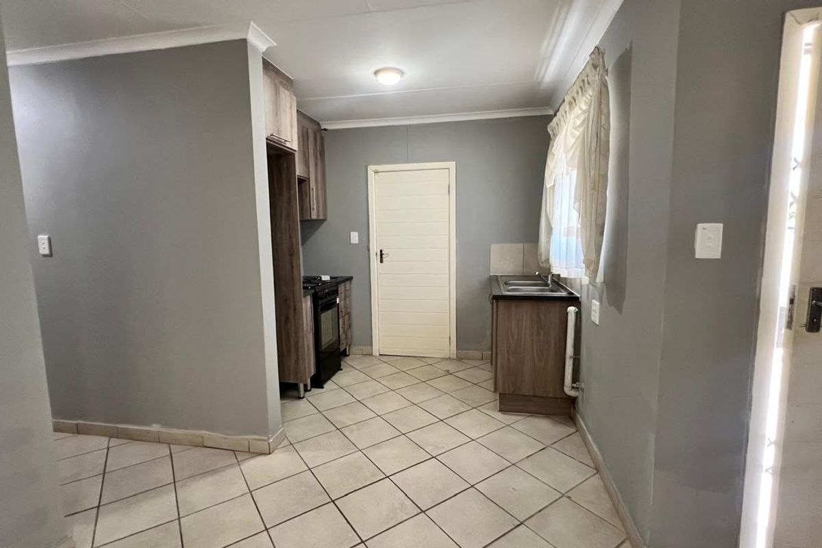 A functional kitchen featuring wood-look cabinetry, tiled flooring, a stainless steel sink, and a freestanding stove, with neutral grey walls.