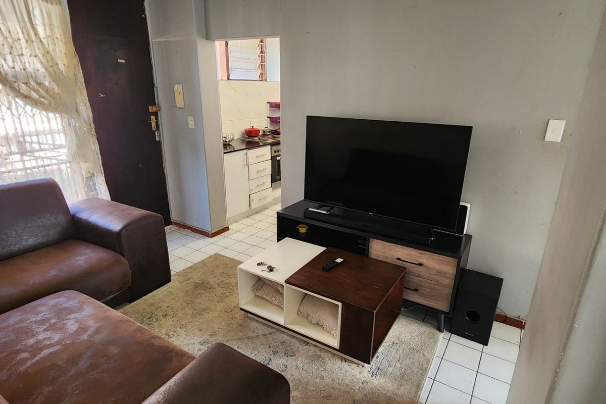 A living room area featuring tiled flooring and a view through to the kitchen, providing a functional open-plan layout.