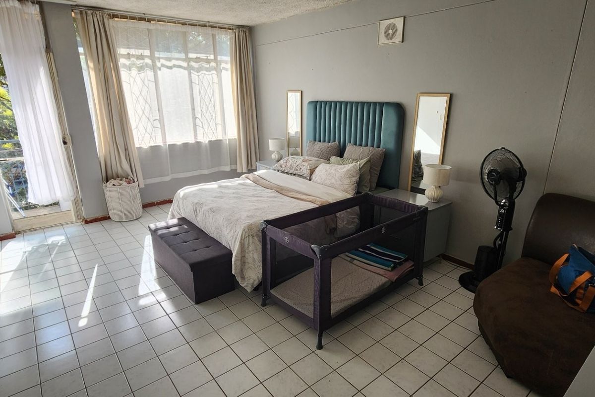 Spacious bedroom featuring tiled flooring, built-in cupboards, and direct access to a private balcony through a glass door.