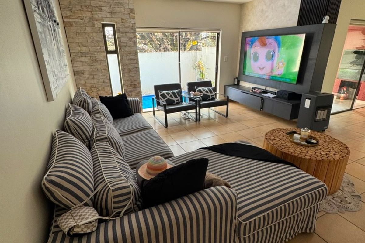 Spacious living room featuring tiled flooring, a stone-clad feature wall, and large sliding glass doors providing direct access to the outdoor pool area.