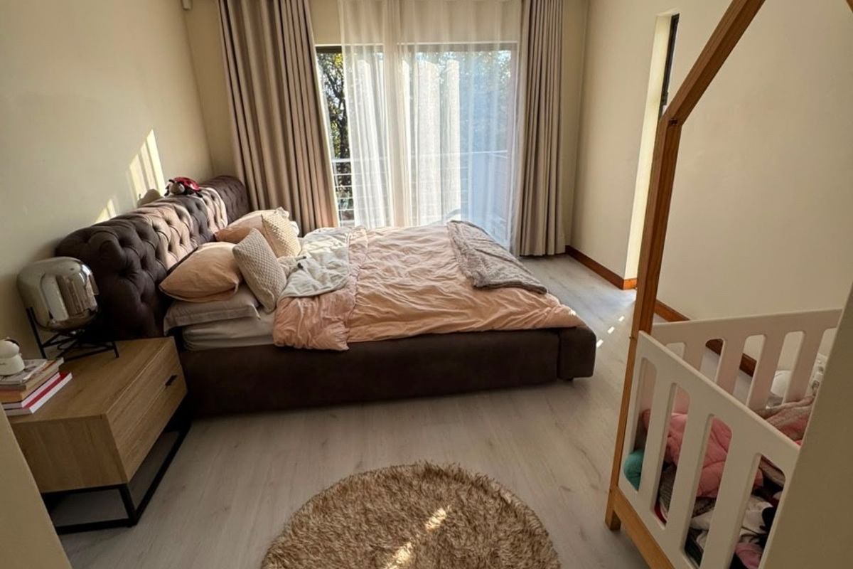 A well-lit bedroom featuring light-toned laminate flooring, a wall-mounted air conditioning unit, and sliding glass doors leading to a balcony.