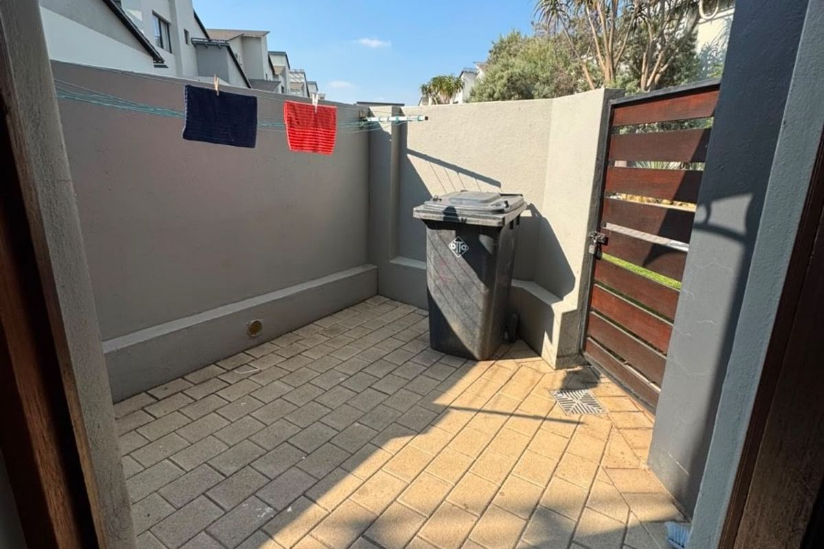 A private paved courtyard area featuring a secure timber gate, perimeter walling, and a wall-mounted clothesline.