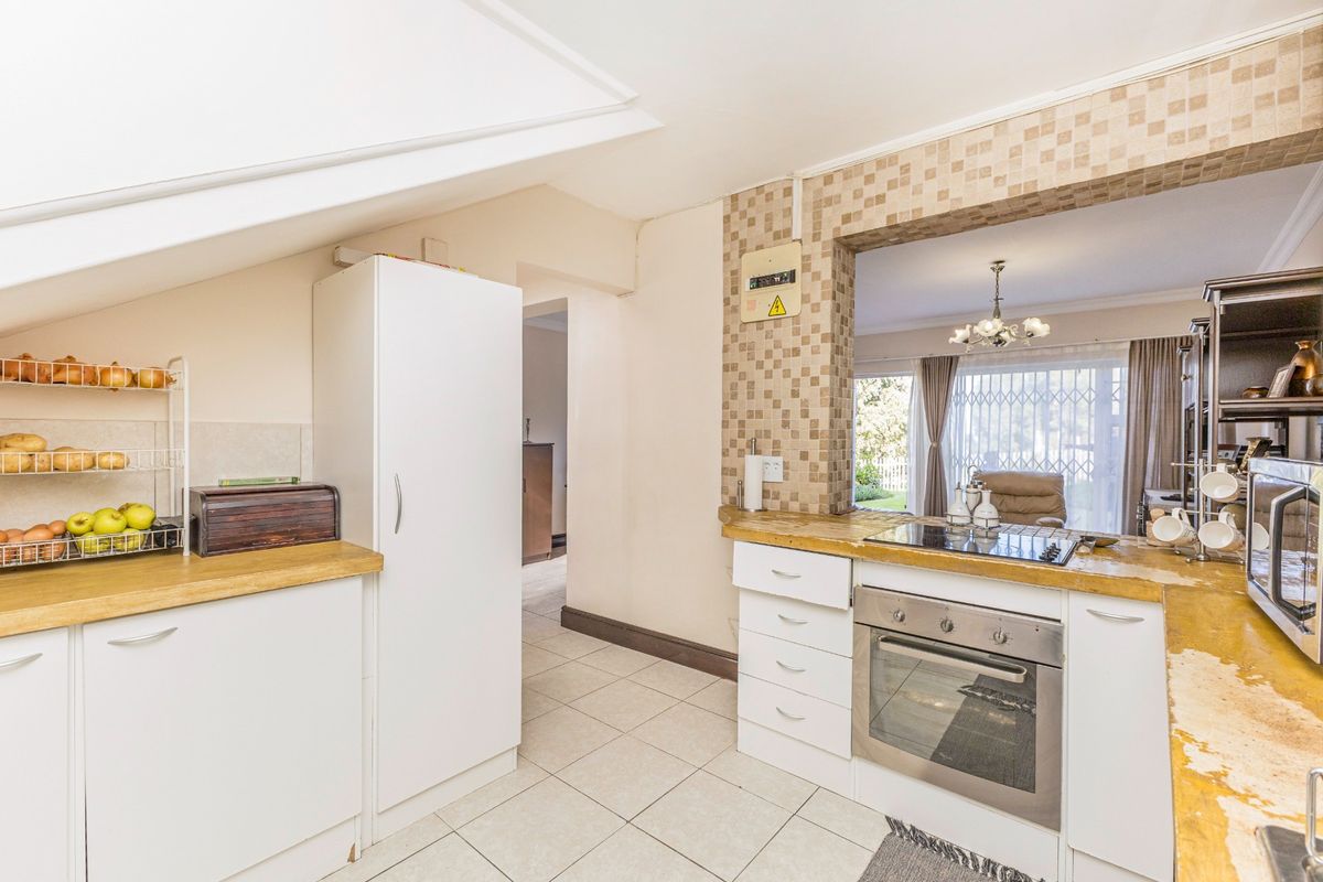 Functional kitchen featuring built-in oven, electric hob, tiled splashback, and ample cabinetry, with a pass-through window overlooking the adjacent living area.
