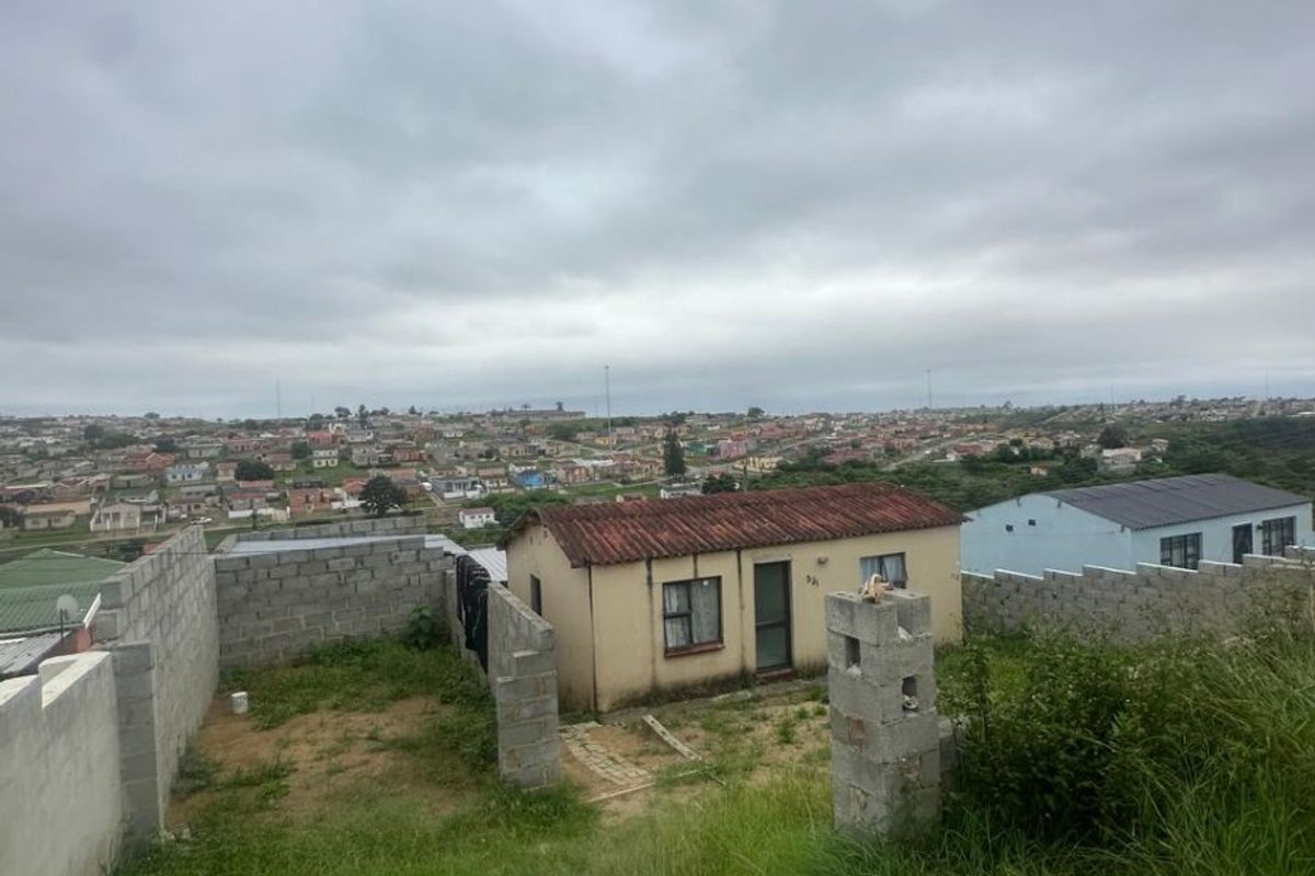 An elevated view of a residential property featuring a detached house with a tiled roof, surrounded by unfinished concrete block boundary walls and open grounds.