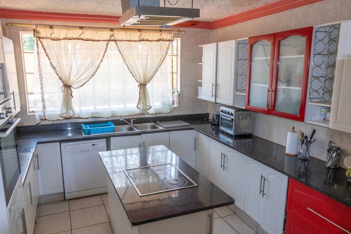 A functional kitchen featuring granite countertops, a central island with a built-in cooktop, and ample white and red cabinetry.