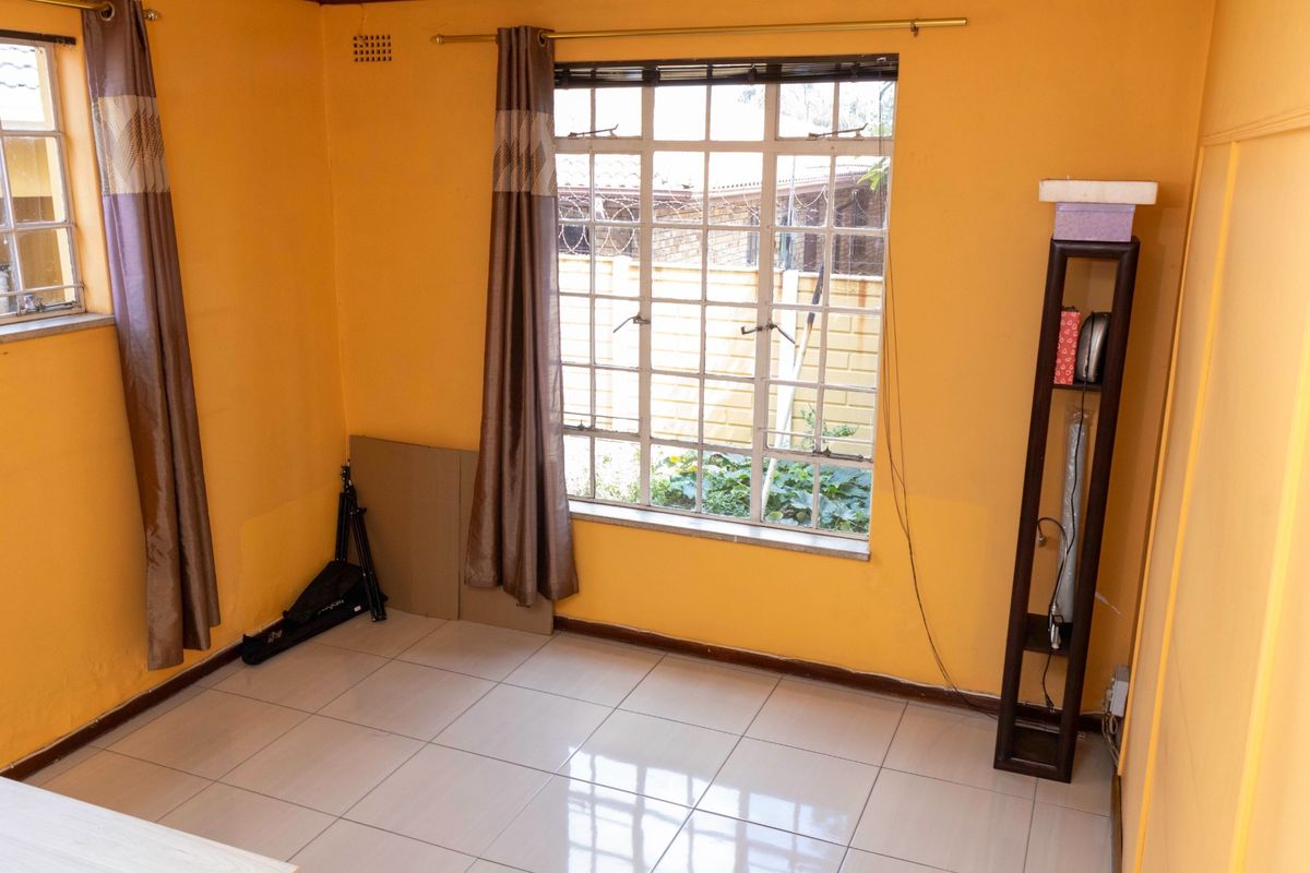 A bedroom featuring tiled flooring, large windows with security bars, and bright yellow wall paint.