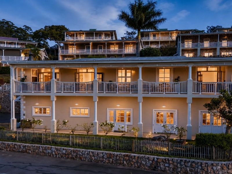 A multi-level townhouse exterior featuring expansive balconies, covered patios, stone retaining walls, and classic architectural detailing illuminated at dusk.