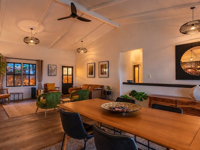 Spacious open-plan living and dining area featuring vaulted ceilings with exposed beams, laminate flooring, and a functional pass-through window to the kitchen.