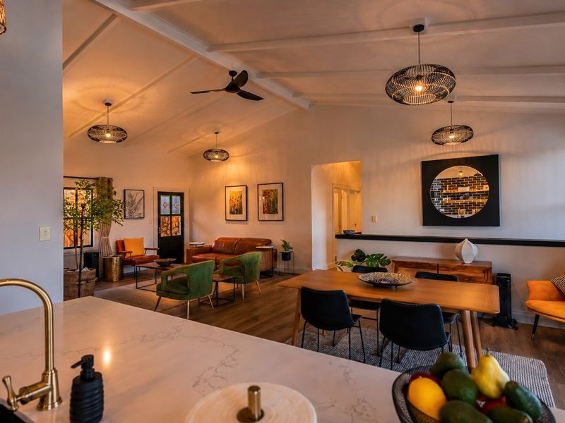 Spacious open-plan living and dining area featuring a vaulted ceiling, modern kitchen with stone countertops, and warm ambient lighting throughout.