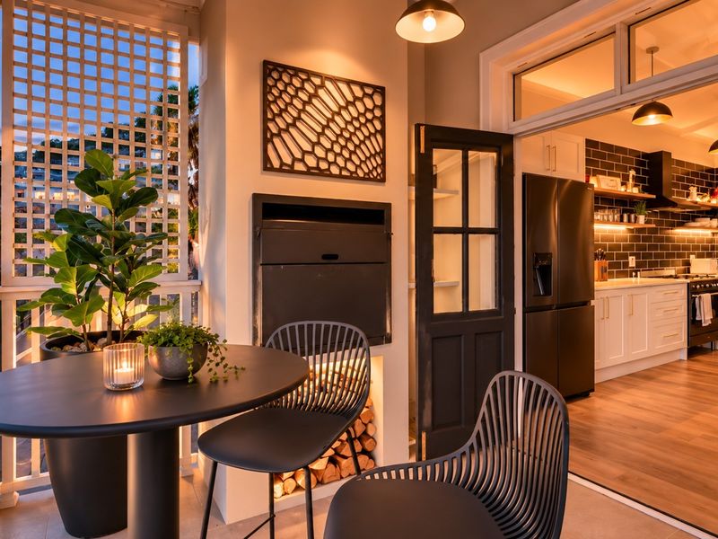 Covered balcony featuring a built-in braai, timber lattice privacy screen, and direct access to the kitchen through classic french doors.