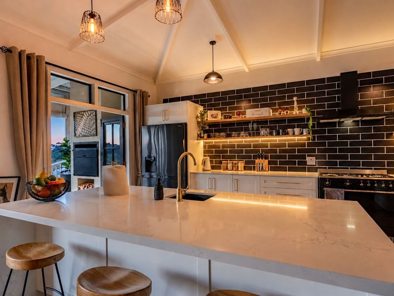 Modern kitchen featuring a large quartz island, brass fixtures, subway tile backsplash, and vaulted ceilings with integrated lighting.