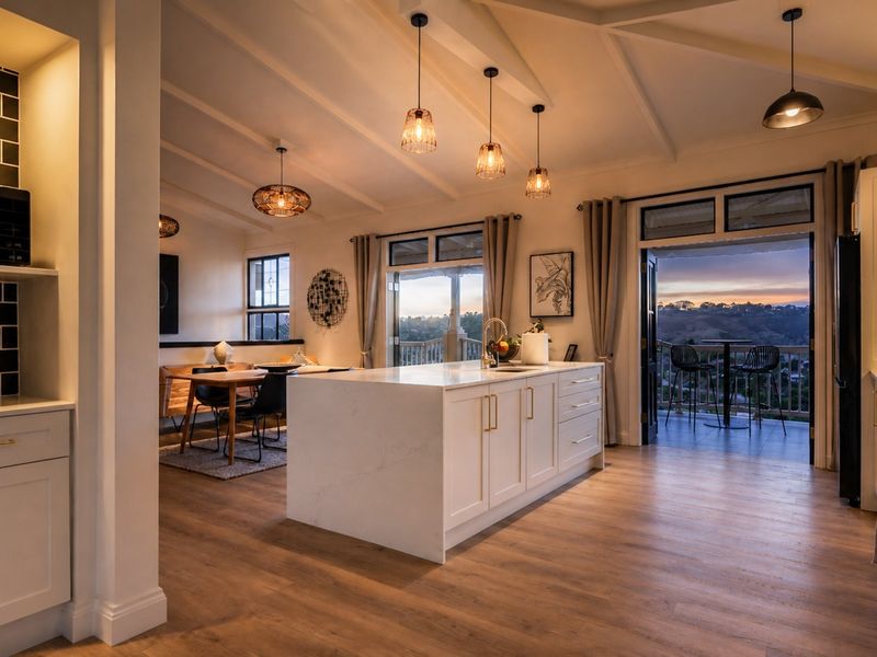 Modern open-plan kitchen and living area featuring a central island, stone countertops, vaulted ceilings, and seamless access to an outdoor balcony with scenic views.