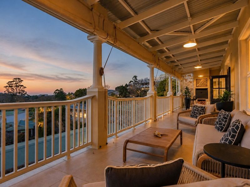 A spacious covered balcony featuring tiled flooring, classic columns, and a built-in fireplace, offering expansive elevated views at sunset.