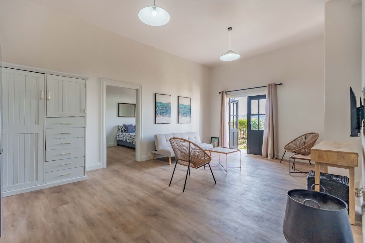 Spacious living room featuring light wood-look flooring, built-in cabinetry, and double doors opening to an outdoor area, with an adjacent bedroom visible.