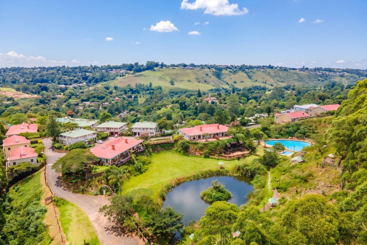 Aerial view of a residential estate featuring multiple townhouse units, a central pond, landscaped grounds, and a communal swimming pool area.