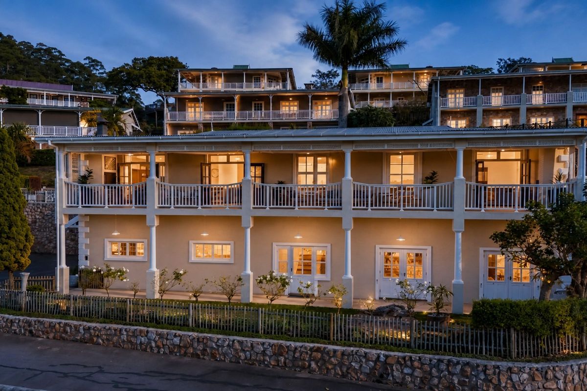 A multi-level townhouse exterior featuring expansive balconies, covered patios, stone retaining walls, and classic architectural detailing illuminated at dusk.