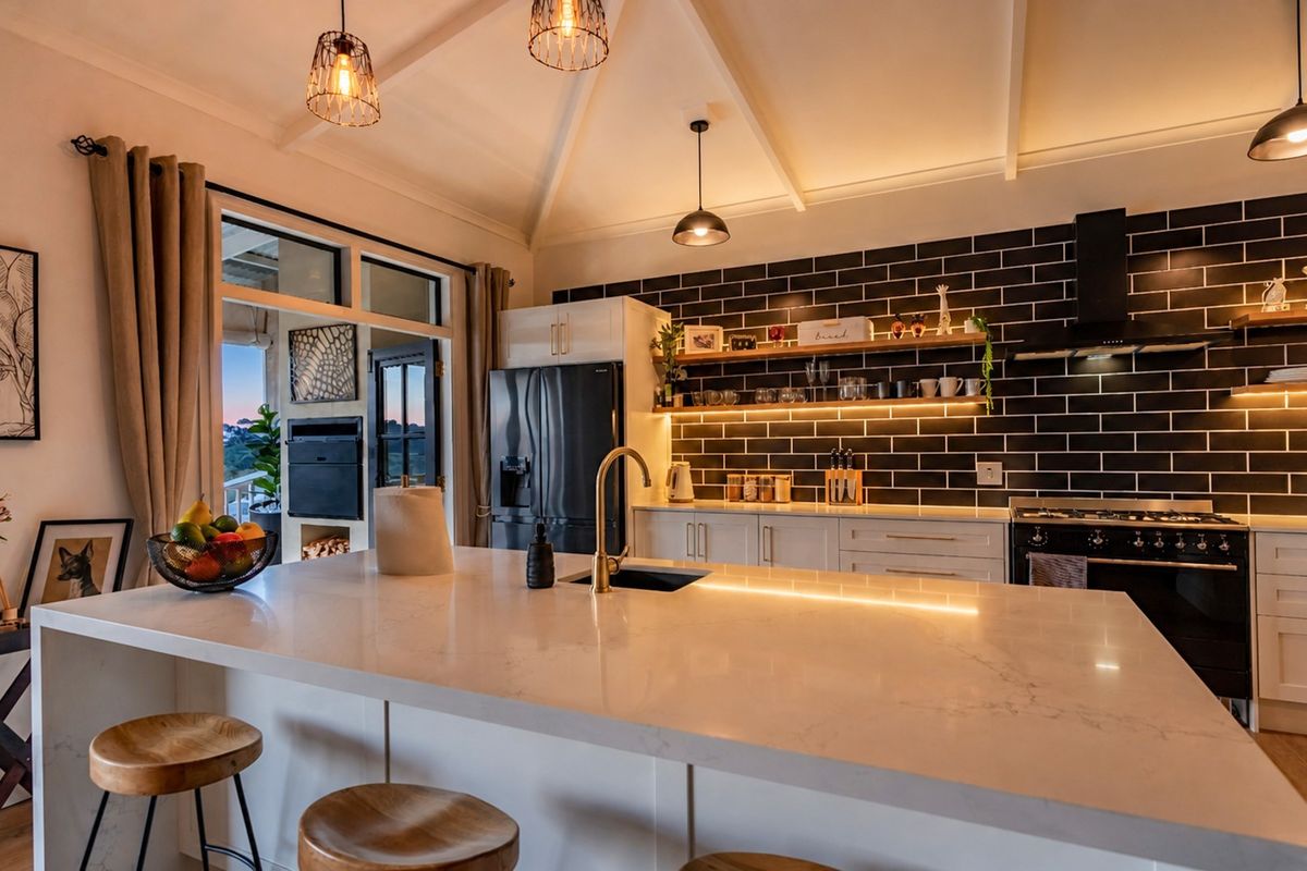 Modern kitchen featuring a large quartz island, brass fixtures, subway tile backsplash, and vaulted ceilings with integrated lighting.