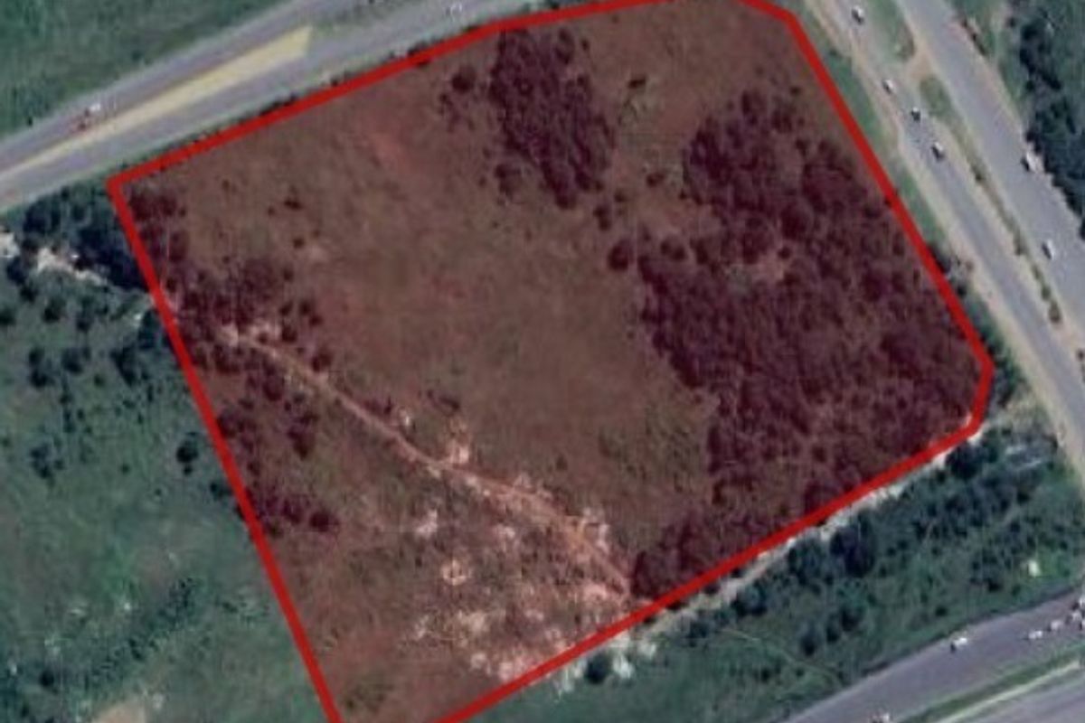 Aerial view of a vacant residential plot with red boundary lines, situated near major road infrastructure.