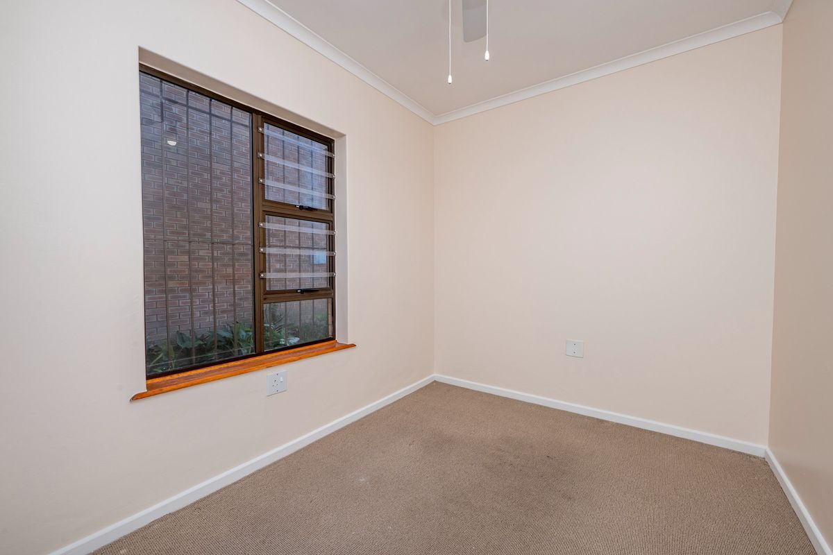 A vacant bedroom featuring neutral walls, carpeted flooring, a ceiling fan, and a window fitted with security bars.