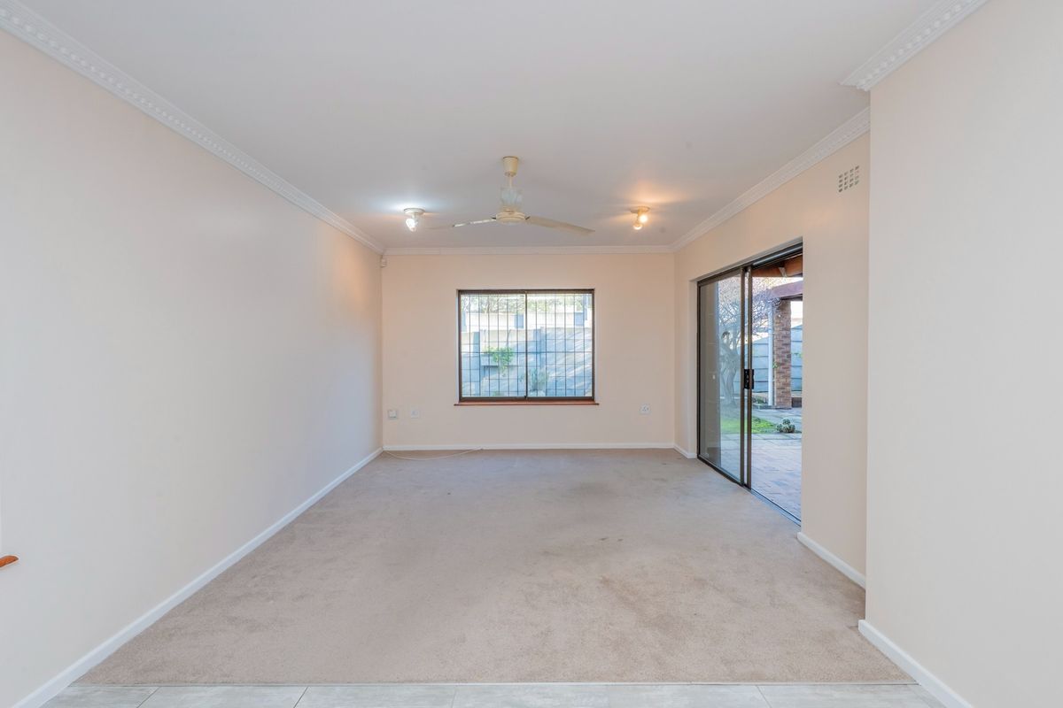 A spacious, empty living room featuring neutral walls, a ceiling fan, and sliding glass doors providing access to an outdoor patio area.