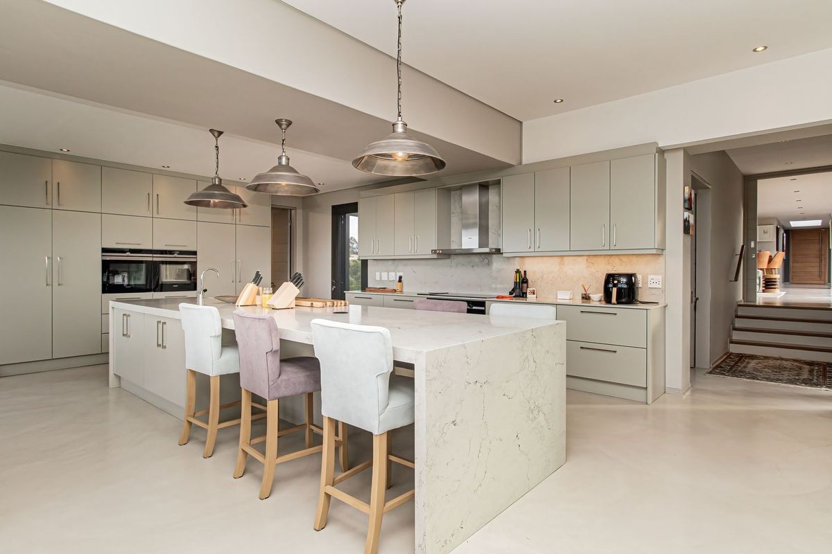 Modern, spacious kitchen featuring a large stone-topped island, integrated cabinetry, built-in appliances, and elegant pendant lighting in a neutral, contemporary design.