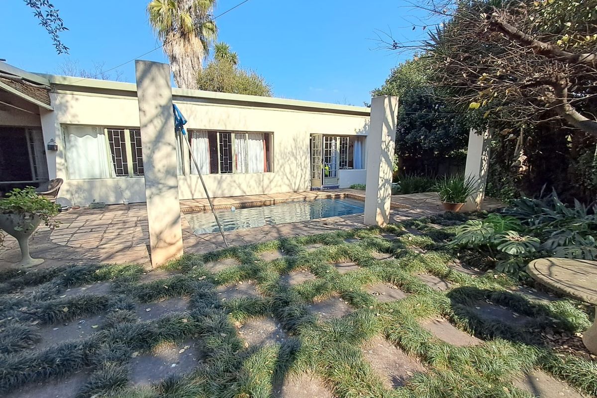 Rear exterior view featuring a swimming pool, paved patio area, and established garden with mature trees.