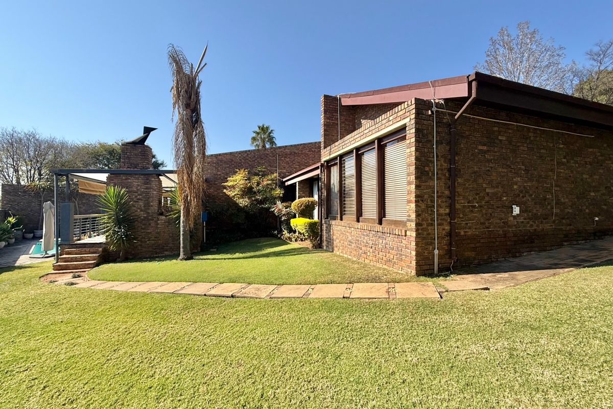 Rear exterior view featuring a face brick facade, covered patio with an outdoor fireplace, and a well-maintained lawn with stone pathways.