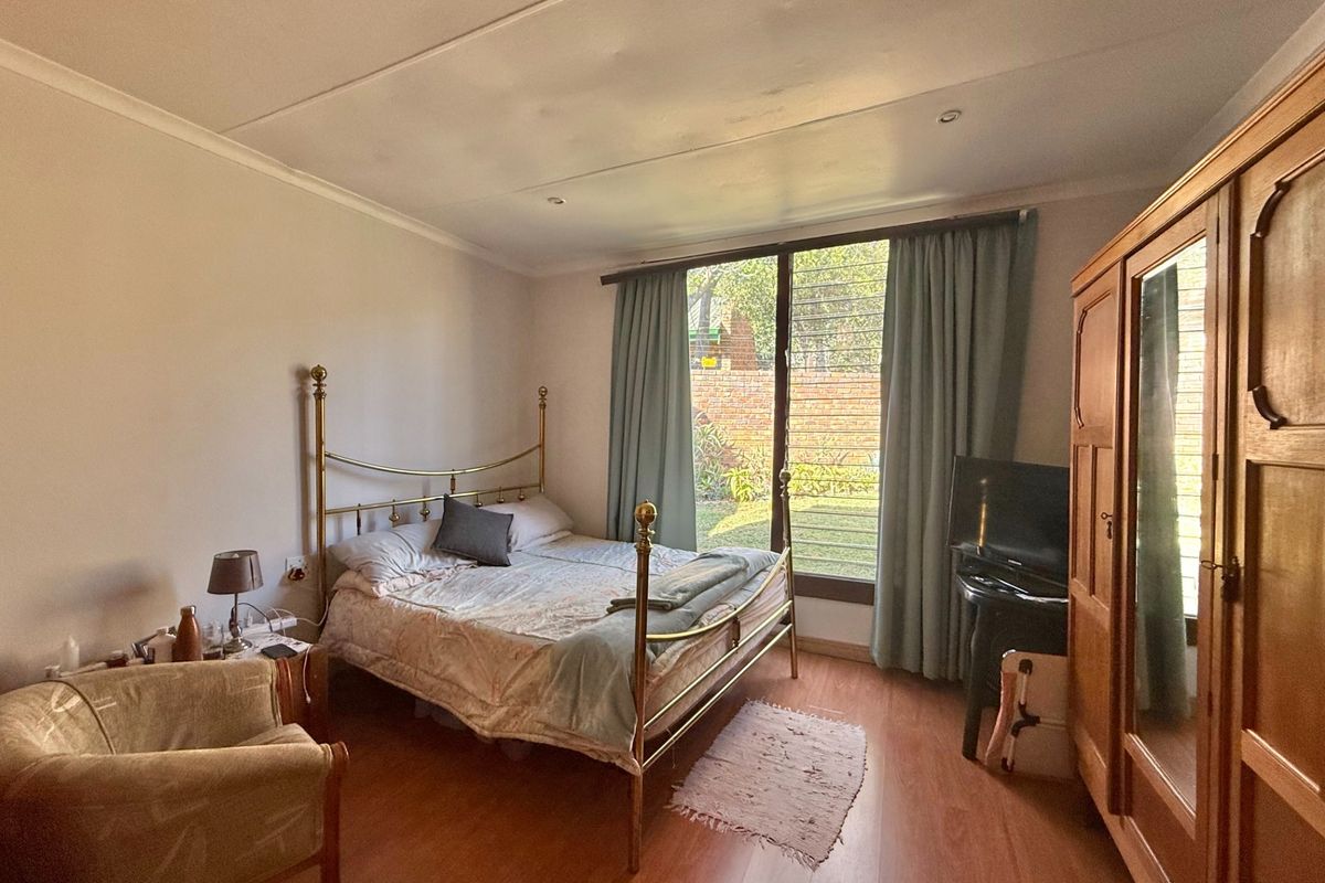 A bedroom featuring laminate flooring, recessed ceiling lighting, and a large window providing natural light and garden views.