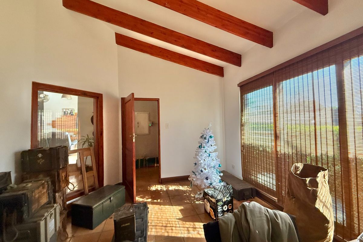 A living area featuring exposed timber ceiling beams, tiled flooring, and large sliding glass doors that provide natural light.