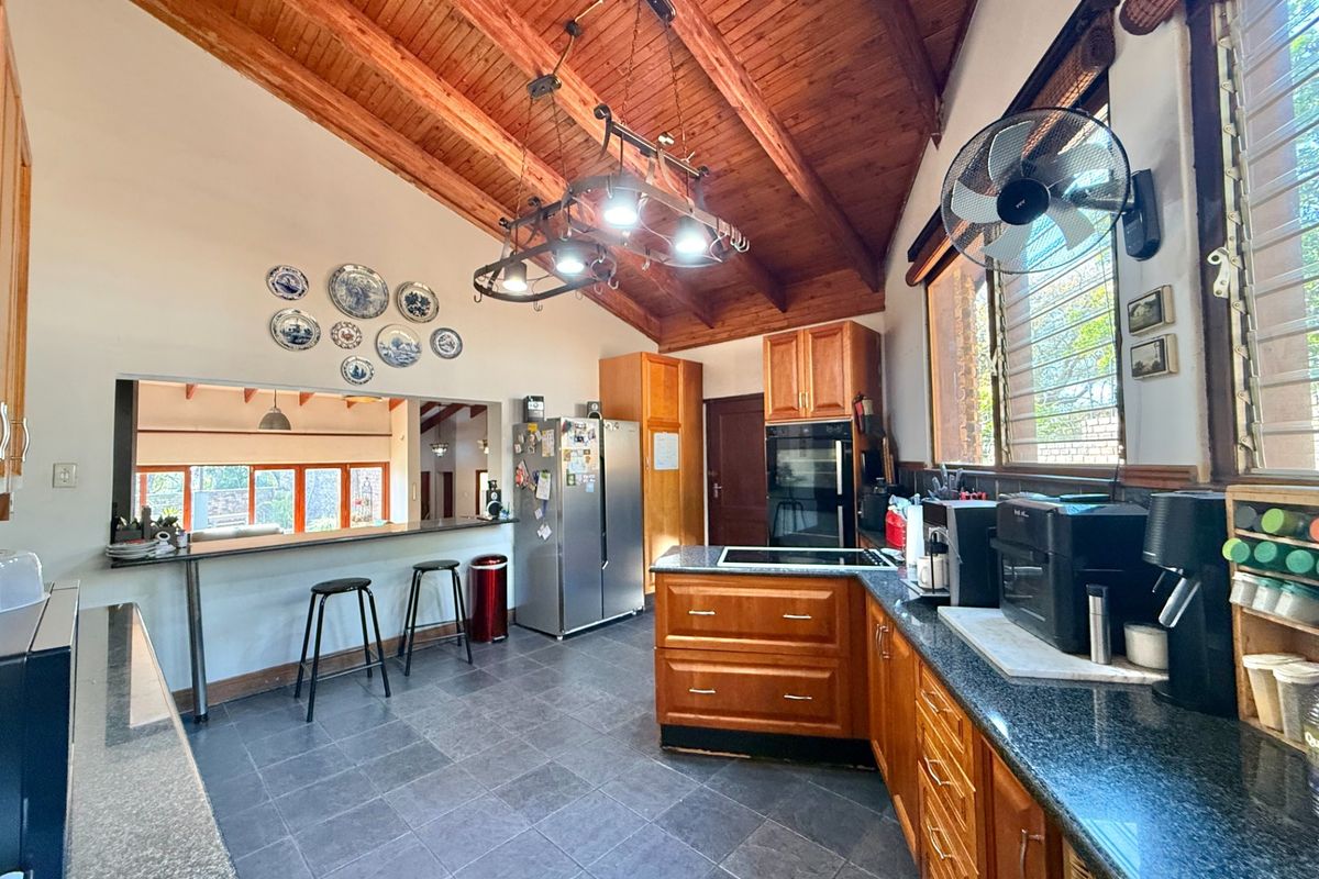 Spacious kitchen featuring timber vaulted ceilings, granite countertops, wooden cabinetry, and a breakfast bar overlooking the living area.