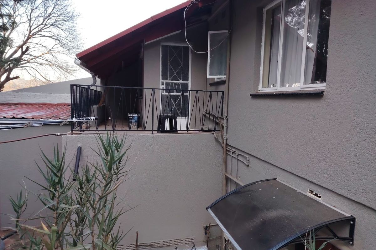 Rear exterior view of the property featuring a raised balcony with metal railing, textured wall finish, and a small protective awning over a lower entrance.