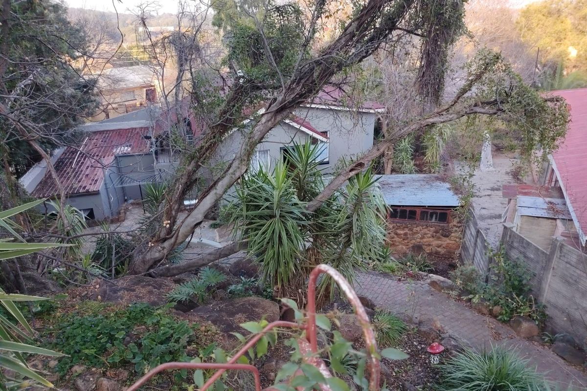 An elevated view of the property grounds featuring multiple structures with red metal roofing, stone masonry elements, and established garden pathways.